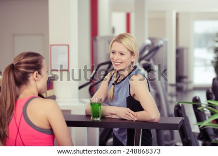 Two young woman relaxing over drinks at the gym enjoying a healthy energy drink after their workout in a health and fitness concept