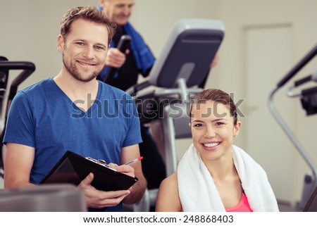 Handsome young trainer with a pretty girl at the gym working out together ion the equipment as he monitors her progress