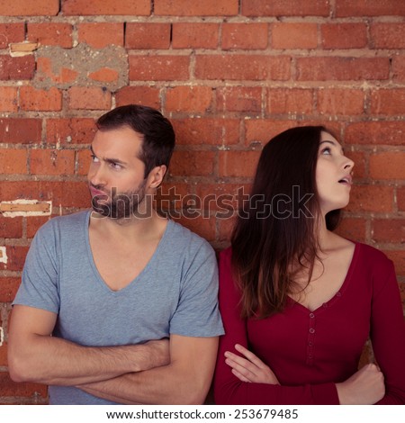 Disgruntled couple ignoring one another after an argument standing looking in opposite directions with folded arms