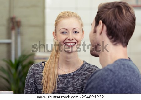 Pretty smiling blond woman chatting to her husband or sweetheart smiling at the camera with a beaming friendly smile, view over the mans shoulder