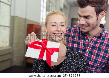 Young man surprising his sweetheart with a gift wrapped in a large red bow to express his love on Valentines Day or their anniversary