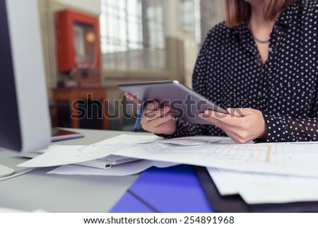 Office Woman Using her Tablet Device While Sitting at her Desk with full of Documents.