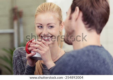 Smiling pretty woman drinking coffee as she chats with her husband smiling happily at him over the rim of the mug