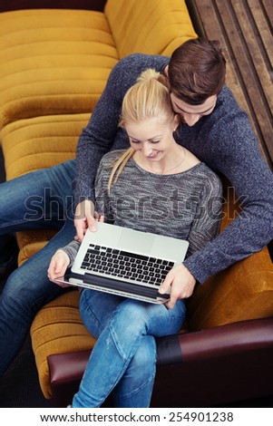 Young couple browsing the internet together sharing a laptop computer as they relax on a sofa, high angle view