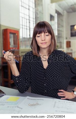 Businesswoman sitting at a desk looking over a report with a pen in her hand as she checks graphs and statistics