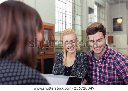 Attractive couple in a meeting with a broker or agent sitting across the desk from her smiling as they read through a presentation