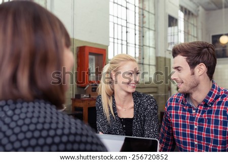Young couple in a meeting with a broker or agent turning to smile at each other , view over the shoulder of the agent