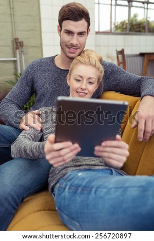Affectionate couple relaxing with a tablet-pc reclining on the sofa at home together sharing the screen