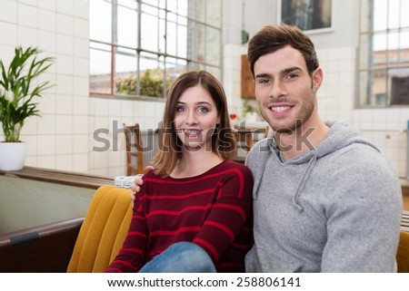 Close up Smiling White Young Couple in Casual Clothing Sitting on Couch While Looking at the Camera.