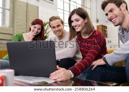 Handsome and Pretty Young White Friends Sitting on the Couch, Watching Something at Laptop Computer Happily.
