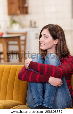 Close up Pretty Smiling White Woman Sitting on Couch and Hugging her Knees While Looking to her Upper Right Side.