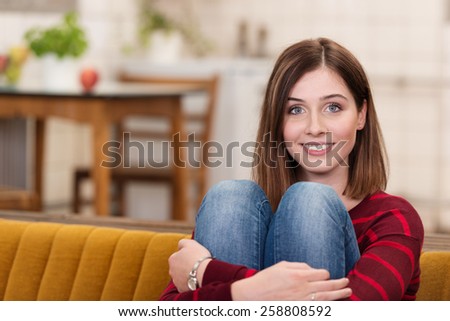 Close up Attractive Young Woman Hugging her Knees at the Couch While Smiling at the Camera.