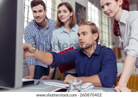 Young man pointing out something on his computer monitor to a group of young business colleagues in a teamwork and leadership concept