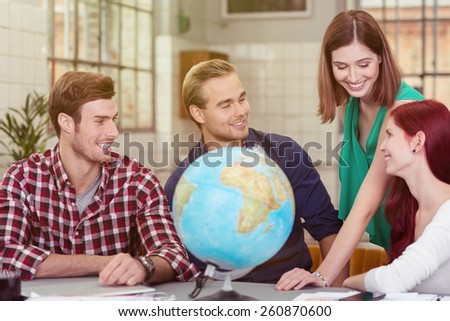 Group of Four Happy Young Friends Talking at the Worktable with Desk Globe
