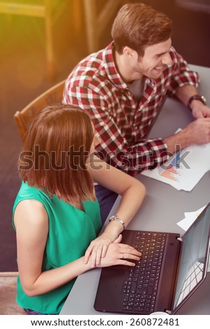 Aerial View of Two Happy Young Friends Sitting at the Table, with Laptop Computer and Documents, Looking to the Right.