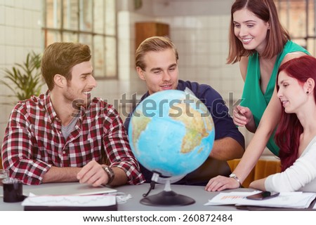 Group of Young Happy Friends Looking at the Globe on Top of the Table