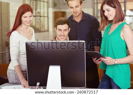 Group of Young Smiling Friends Watching Something at the Computer Screen Together Inside the Office.
