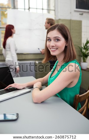Close up Pretty Young Woman in Green Sleeveless Top Sitting at the Table with Laptop Computer While Smiling at the Camera.