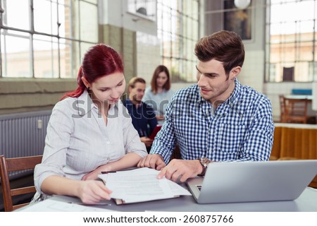 Young business team, a man and woman, working in the office sitting at a desk discussing paperwork