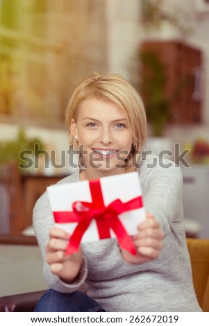 Excited young woman showing off her Valentines gift holding it in front of her with a joyful smile displaying the decorative large red ribbon