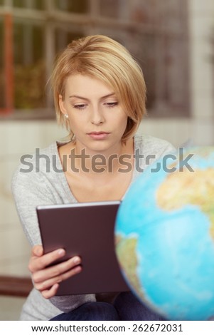 Close up Young Pretty Blond Woman Behind the Globe Looking at the Screen of her Tablet Computer on her Hand.