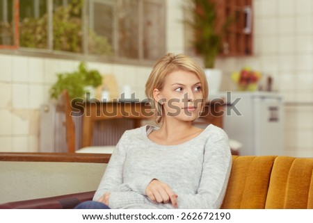 Young Pretty Blond Woman in Casual Clothing Sitting on the Sofa While Looking to the Right Of the Frame Seriously.