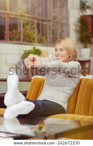 Relaxed attractive young woman stretching in contentment as she relaxes on a couch in the living room smiling with pleasure