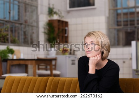 Thoughtful Pretty Young Woman with Short Blond Hair, Wearing Black Long Sleeve Shirt, Sitting on the Couch at the Living Room.