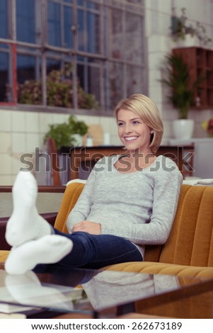 Smiling attractive young woman relaxing at home on a comfortable sofa with her shoes off and feet up on the coffee table