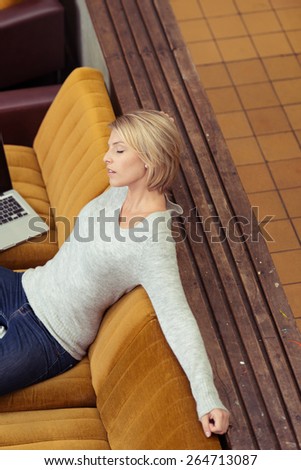 Aerial View of a Blond Young Woman Taking a Nap While Leaning on the Dark Yellow Sofa at the Living Area.