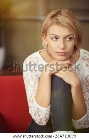Close up Pretty Blond Woman Sitting on Red Sofa Leaning on her Knee While Looking to the Right of the Frame Seriously.