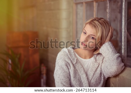 Sad young woman sitting thinking resting her head on her hand on the back of the sofa as she stares at the ground with a serious expression