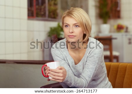 Contemplative young woman drinking coffee clutching a mug on her hands as she stares ahead of her with a serious distracted expression, with copyspace indoors at home