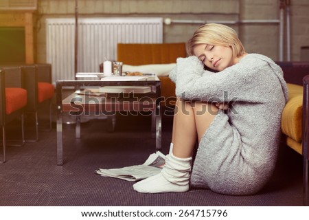 Tired young woman relaxing at home sitting on the floor with her knees drawn up as she rests her head on her hands and eyes closed