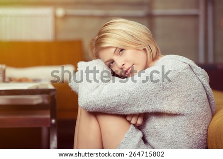 Serious depressed young woman relaxing at home with her head resting on her drawn up knees looking at the camera