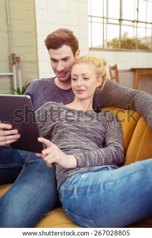 Close up Young Romantic Couple Sitting at the Brown Sofa Watching Something at the Tablet Computer Together While Girlfriend Leaning to her Boyfriend.