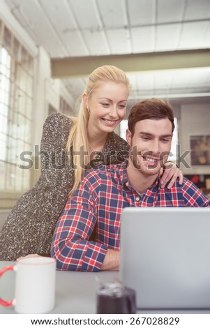 Happy Young Couple Watching a Video Together at the Laptop Computer on Top of the Table