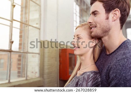 Close up Smiling Young Sweet Couple Watching Outside at the Glass Window While Girlfriend Leaning on the Body of her Boyfriend