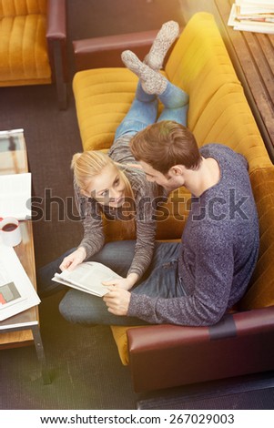 Aerial View of a Sweet Young Couple Relaxing on Living Room Sofa with Newspaper Looking Each Other.