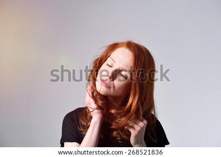 Attractive young redhead woman with a stiff neck standing rubbing it with her hand and eyes closed, over grey