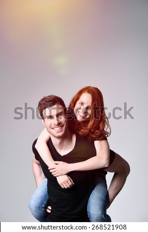 Close up Handsome Man Carrying his Pretty Girl on his Back While Smiling at the Camera. Captured in Studio with Gray Background.