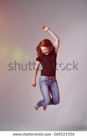Portrait of a Happy Young Girl Doing Jump Shot Pose on a Gray Background with Light Coming From the Left Side of the Frame