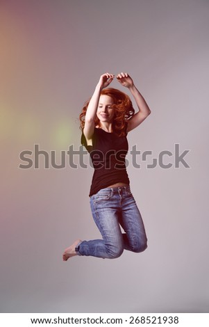 Portrait of an Active Young Woman Wearing Casual Clothing Doing a Jump Shot on a Gray Background with Light From the Left Side.