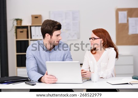 Young Business Couple Sitting at the Table with Laptop Computer and Looking Each Other Seriously