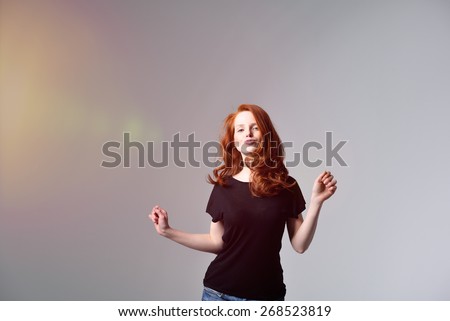 Half Body Shot of a Pretty Red Haired Woman in Motion, Wearing Black Shirt with Pouting Lips, Looking at the Camera on Gray Background.