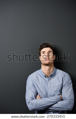 Close up Serious Young Handsome Man in Long Sleeves Shirt Leaning on Gray Wall with Arms Crossed and Looking Up, Emphasizing Texts Space at the Left Side.