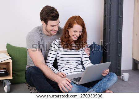 Young Sweet Couple Sitting on the Floor While Watching a Video on Laptop Computer Together.