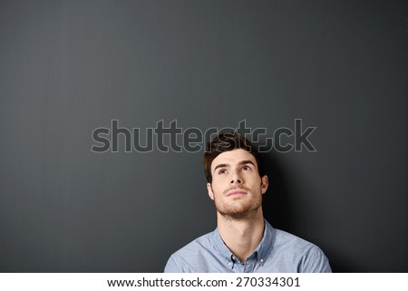 Head and Shoulder Shot of a Thoughtful Young Gorgeous Man Leaning on a Gray Wall While Looking Up, Emphasizing Copy Space.