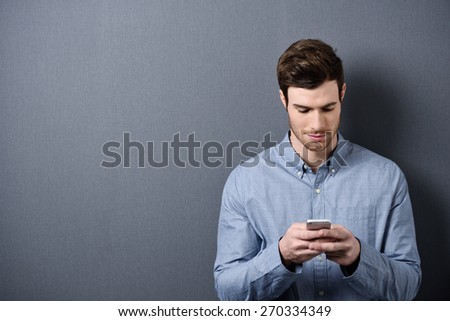 Close up Handsome Young Guy in Blue Gray Long Sleeves Shirt Busy with his Mobile Phone, Isolated on Gray Background with Copy Space on the Left.