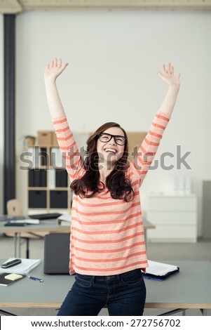 Half Body Shot of a Happy Young Woman Leaning her Back Against the Table, Raising her Two Arms Up High.